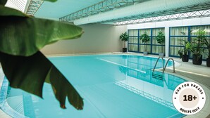 Una piscina interior con vista despejada del área de la piscina, plantas en macetas y un techo con estructura metálica.