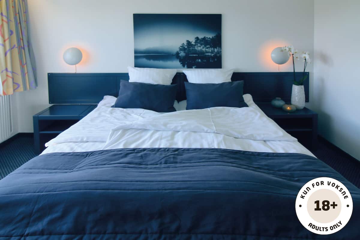 Een hotelkamer met een bed, twee nachtkastjes, een wandlamp, een schilderij en een vaas met bloemen.