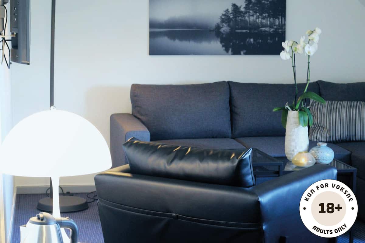 Een moderne woonkamer met een grijze bank, een zwarte leren poef, een witte lamp en een lijst met een foto van een meer.