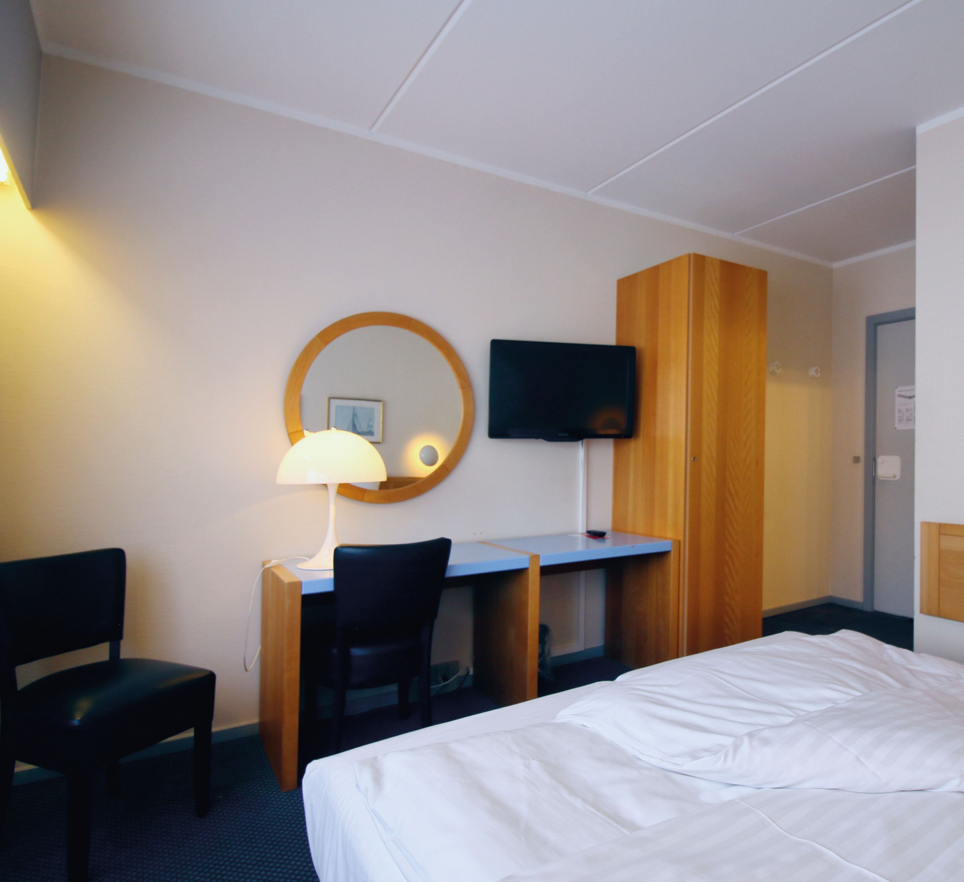 Et hotelværelse med seng, skrivebord, stol, fjernsyn og spejl.