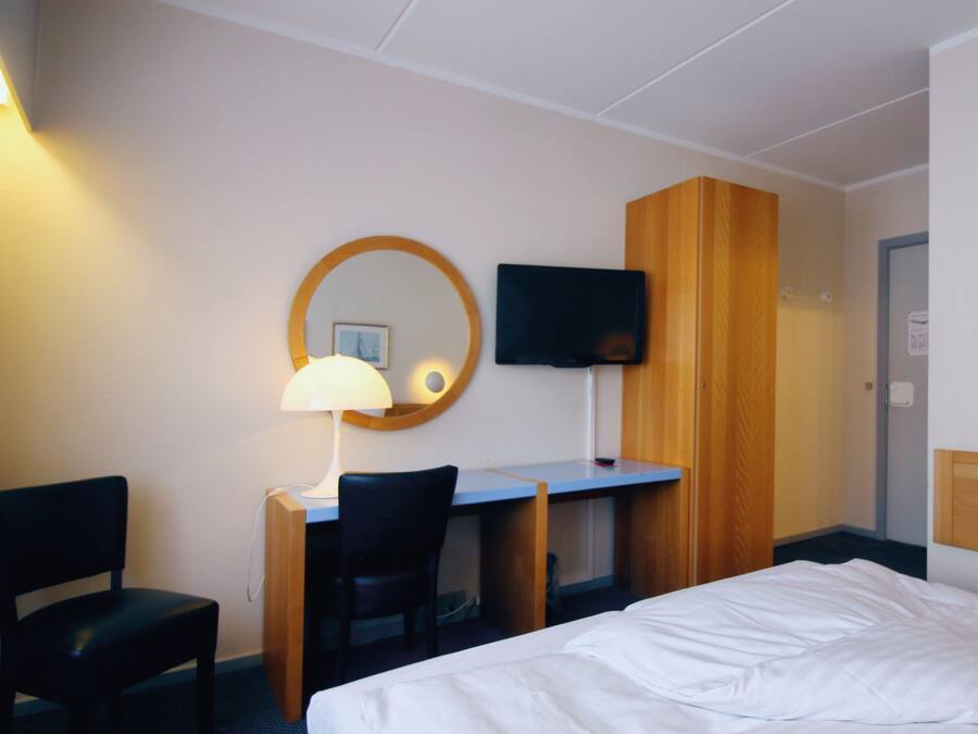 A hotel room with a bed, a desk, a chair, a TV, and a mirror.