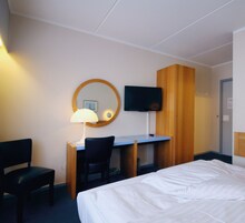 Una habitación de hotel con cama, escritorio, silla, televisor y espejo.