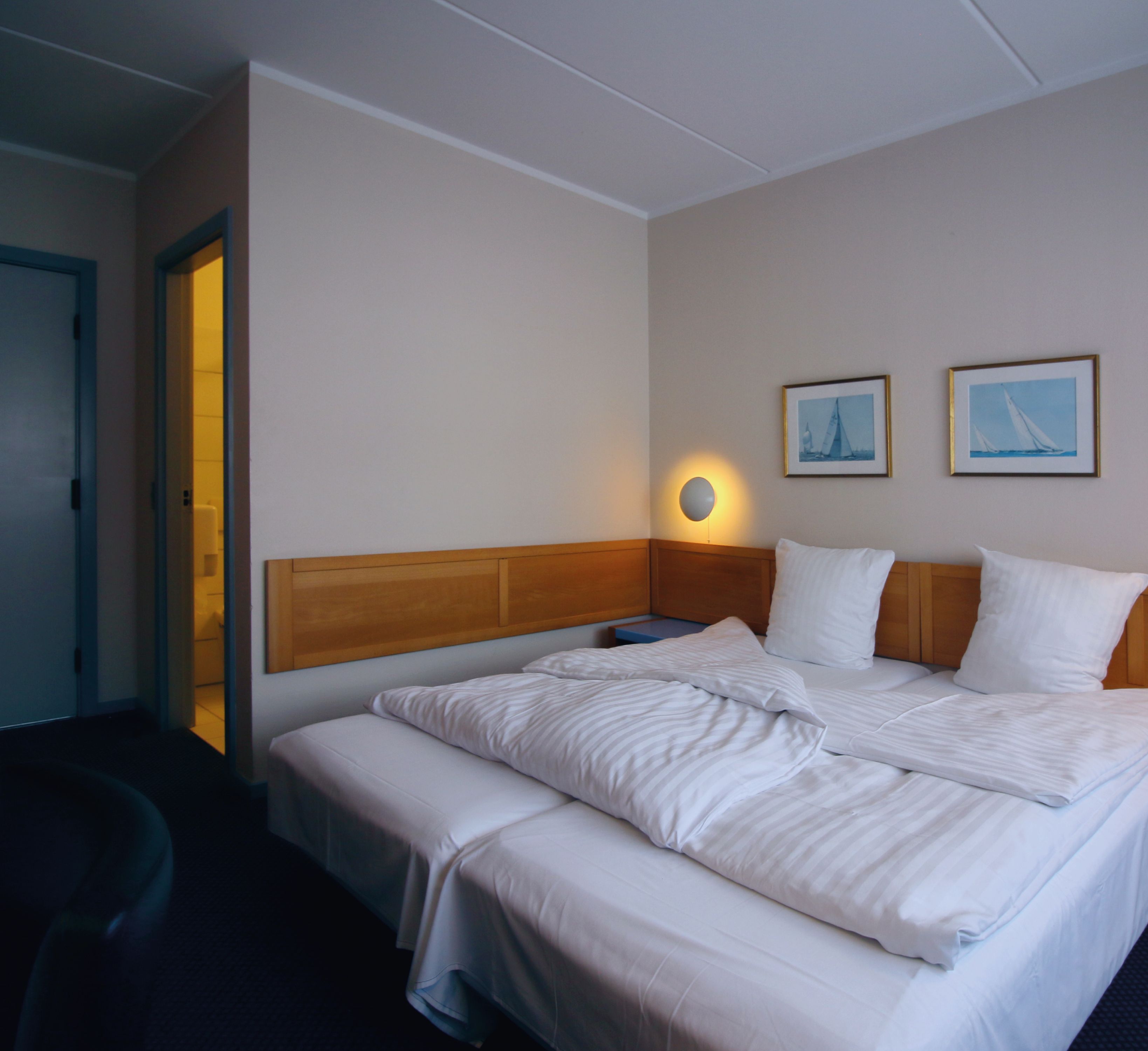 A hotel room with a large bed, two wall-mounted lamps, and two framed pictures.