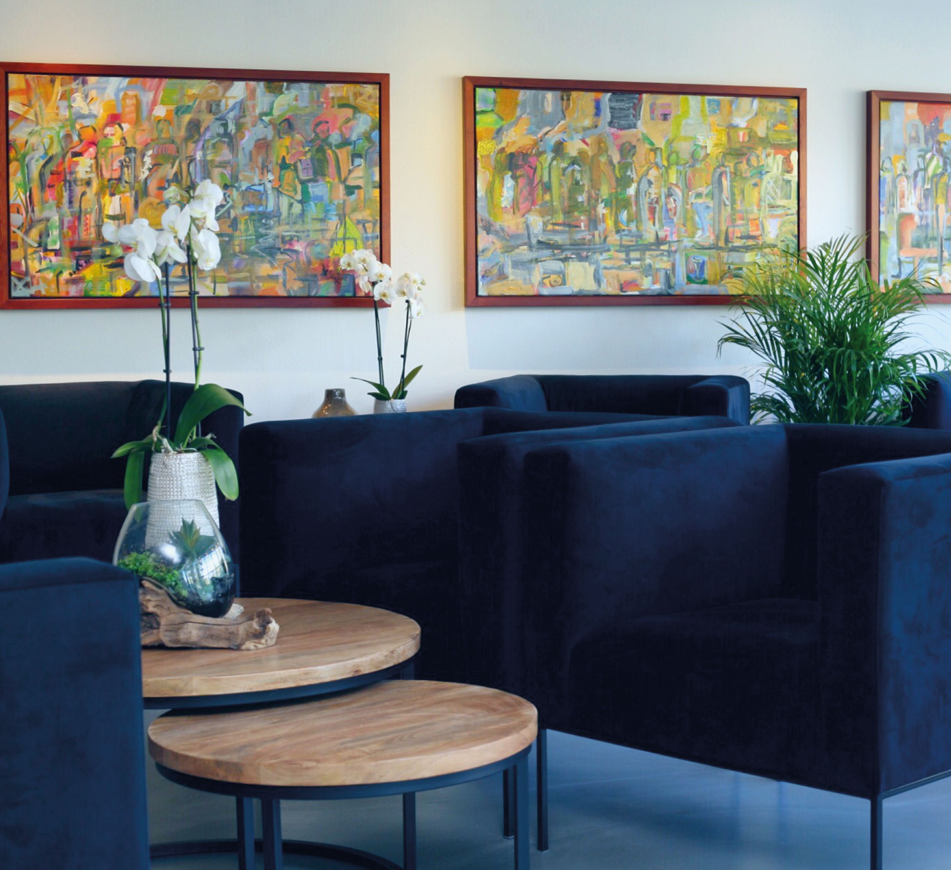 Een moderne lobby met donkerblauwe banken, een ronde houten tafel en drie abstracte schilderijen aan de muur.