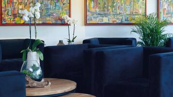 Een moderne lobby met donkerblauwe banken, een ronde houten tafel en drie abstracte schilderijen aan de muur.