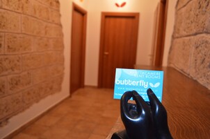 Una mano tiene un biglietto da visita per Butterfly Rooms, con un muro in mattoni e una porta in legno sullo sfondo.