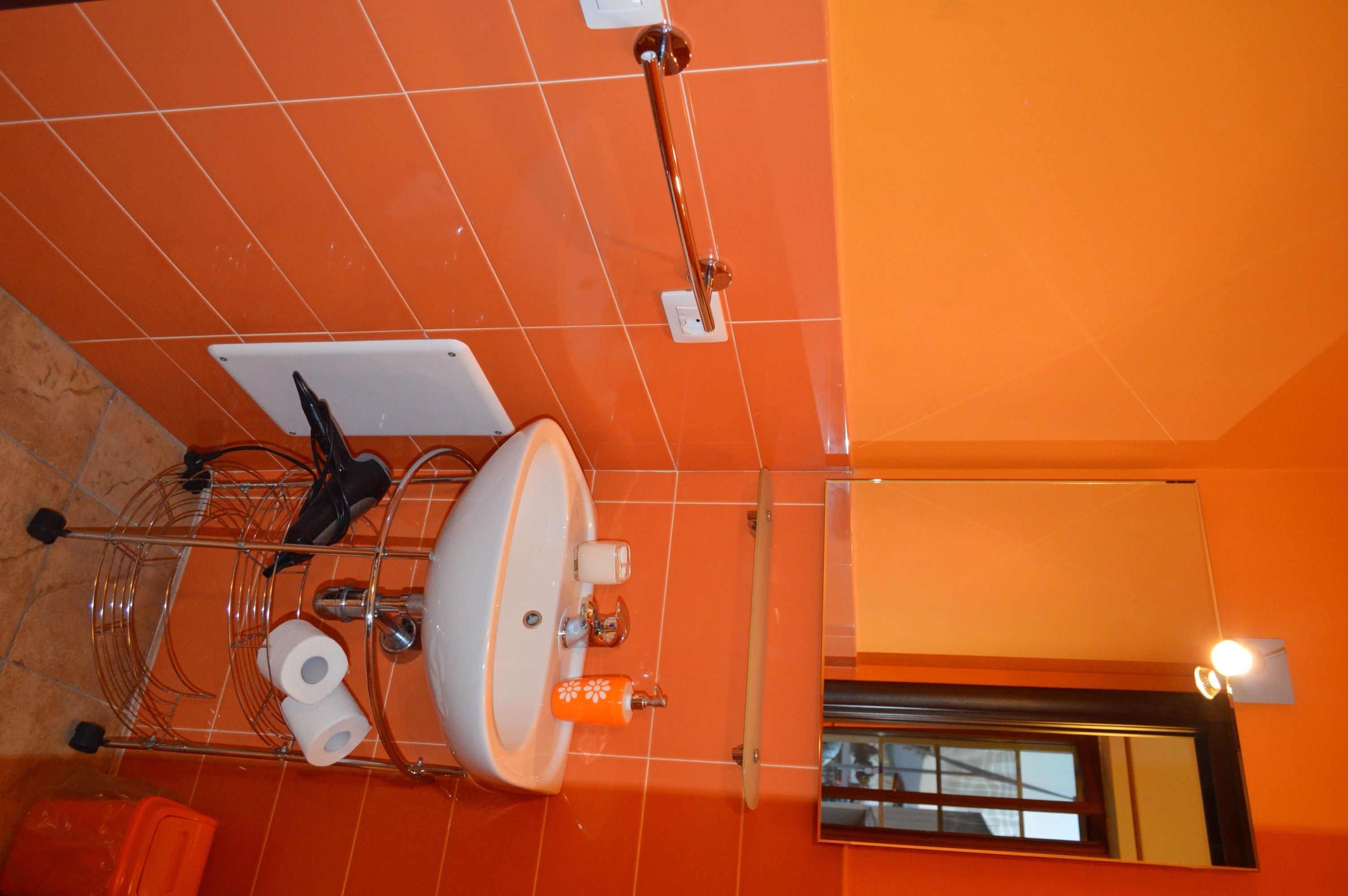 A bathroom with a white sink, orange tiles, a towel rack, a mirror, and a window.