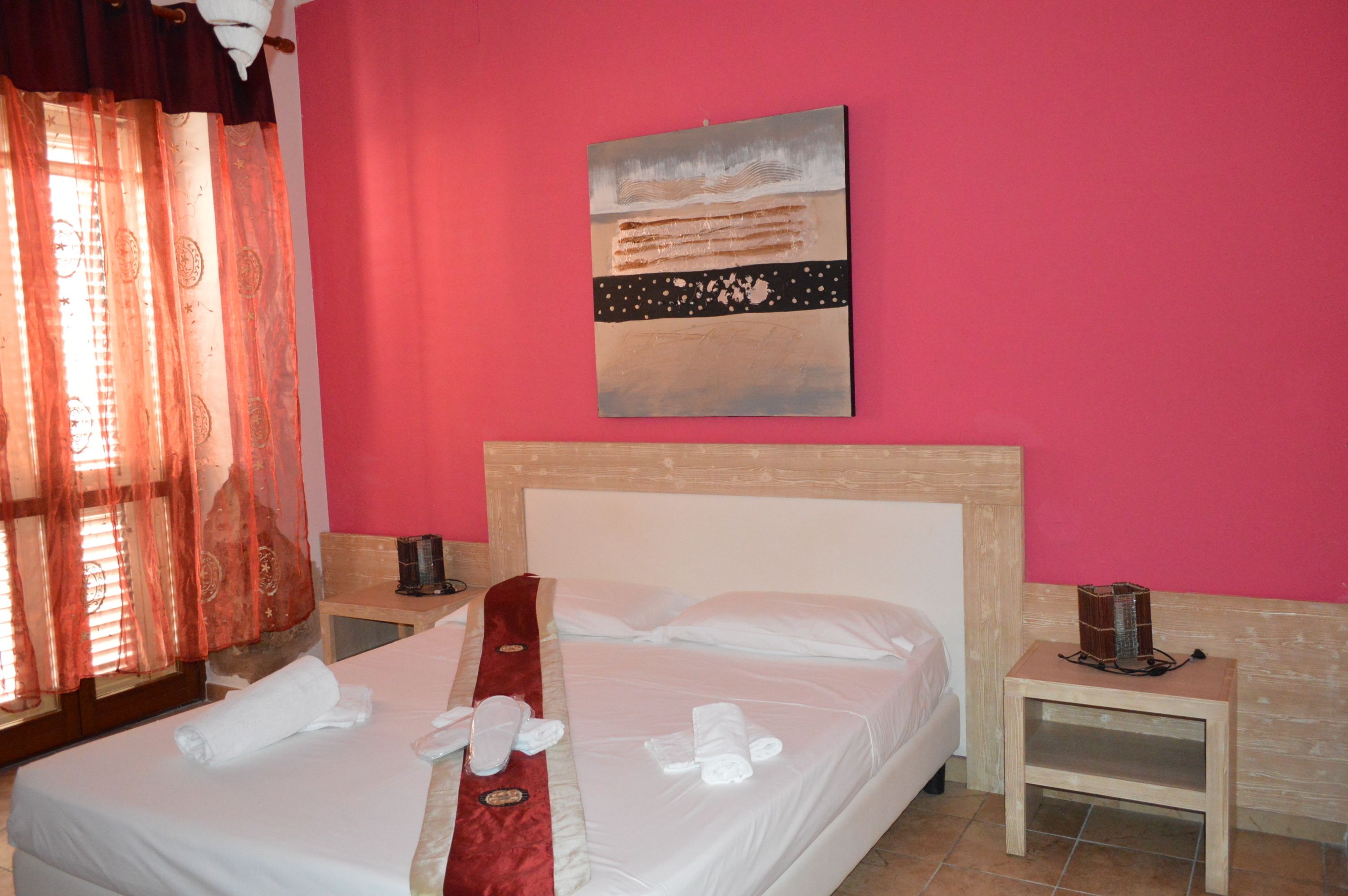Quarto de hotel com cama, um quadro na parede, mesa de cabeceira e janela com cortinas.