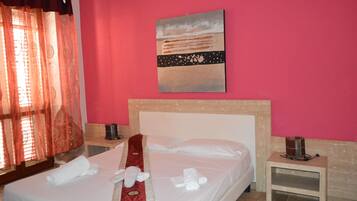 Quarto de hotel com cama, um quadro na parede, mesa de cabeceira e janela com cortinas.