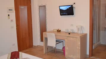A hotel room with a wooden desk, a chair, a television mounted on the wall, a bed with a red and white bedspread, and a bathroom visible through an open door.
