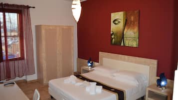 A hotel room with a bed, a wardrobe, a desk, and a painting on the wall.