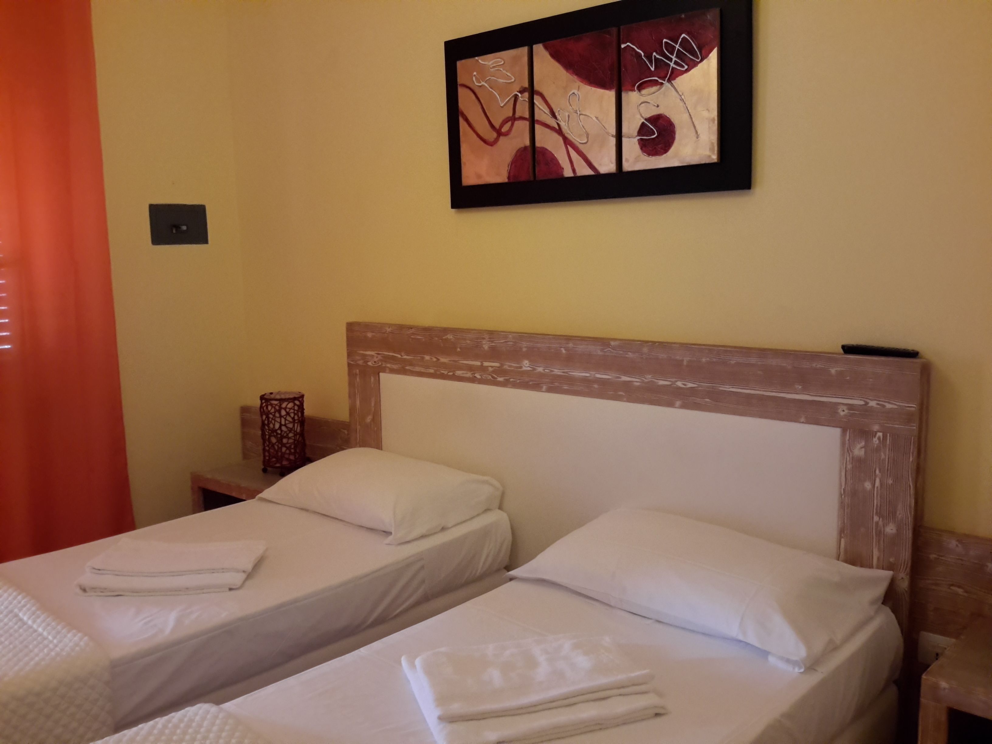 Una habitación con dos camas, cabecera de madera, un cuadro abstracto colgado en la pared y un objeto decorativo en una mesita de noche.