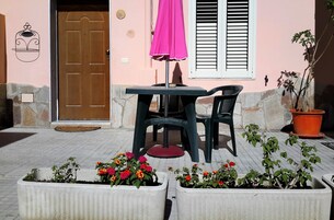 Una terrazza con tavolo e sedie, un ombrellone rosa e piante in vaso.