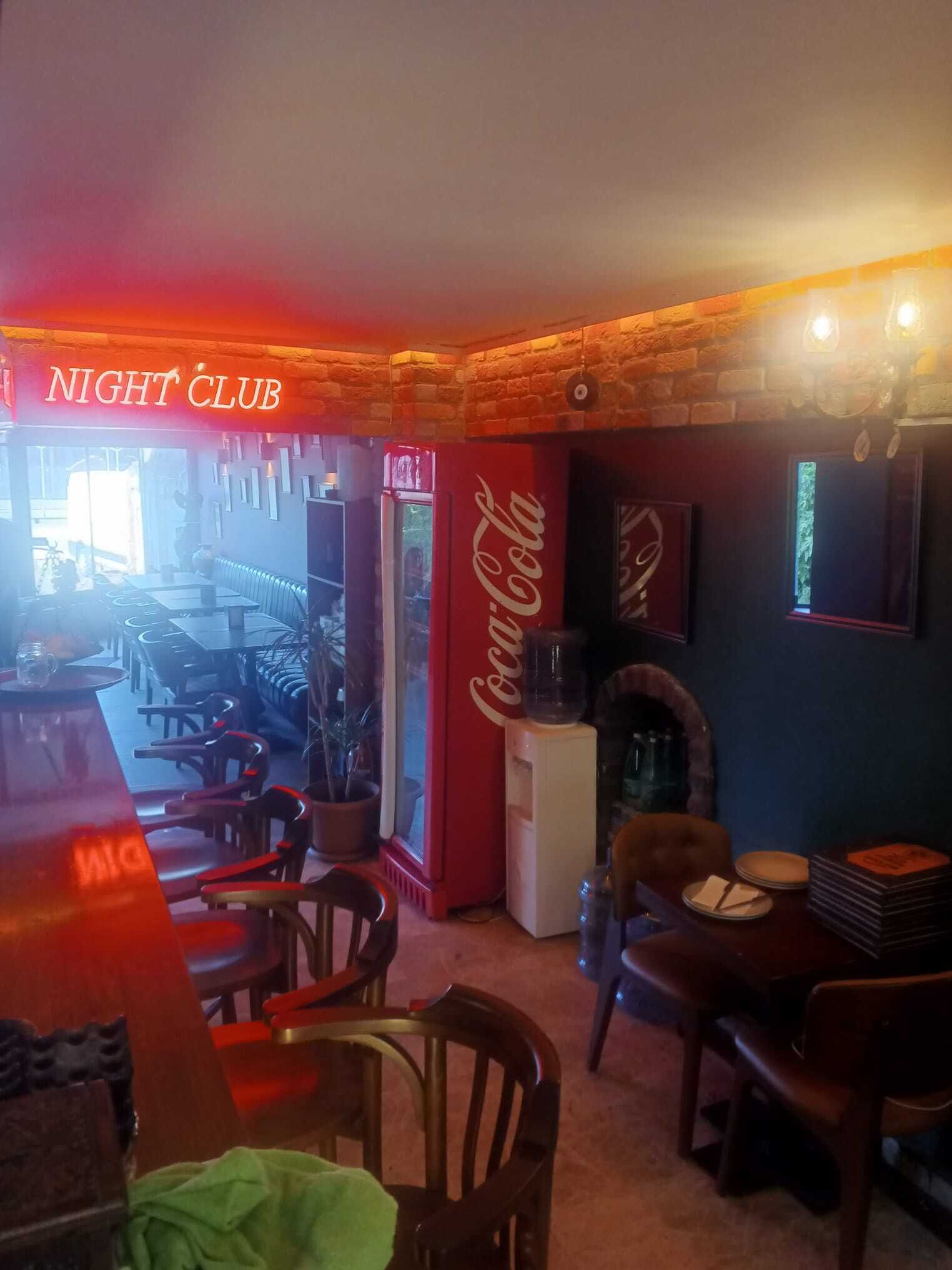 Un interior de discoteca acogedor, con un refrigerador Coca-Cola, mesas y sillas de madera.