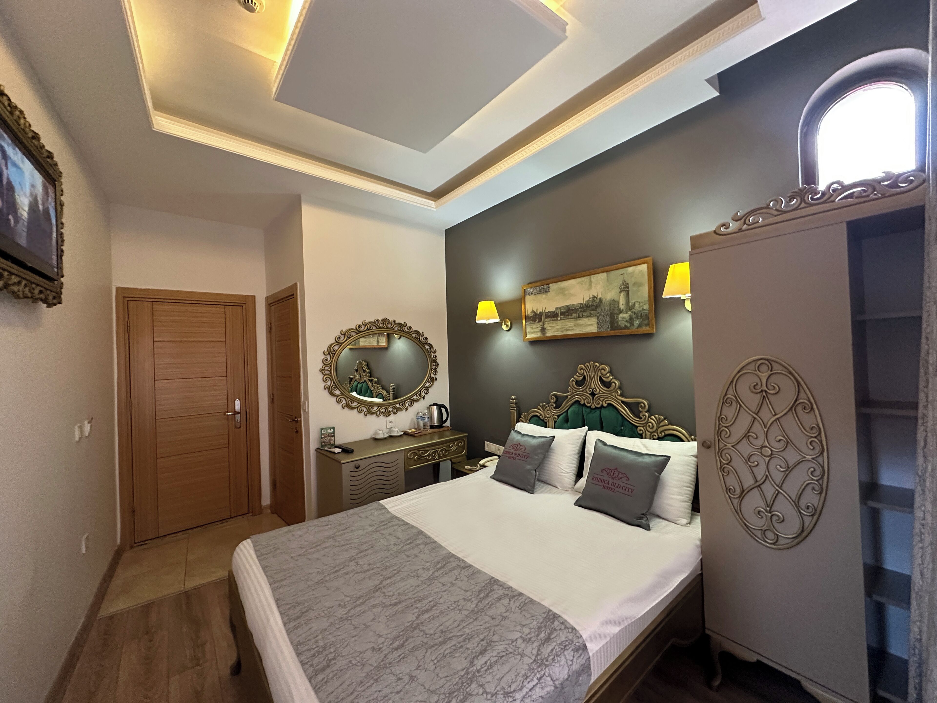 A bedroom with a bed, a dresser, a mirror, a painting, and a ceiling light fixture.