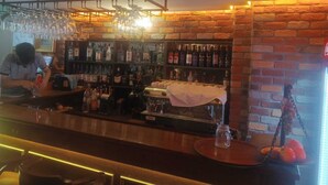 Un espace bar avec des étagères remplies de bouteilles d’alcool, un comptoir avec une caisse enregistreuse et des verres suspendus.