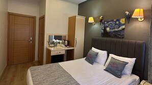 Une chambre d’hôtel moderne avec un grand lit, des tables de chevet, un bureau avec une lampe, un tableau au mur et un luminaire au plafond.