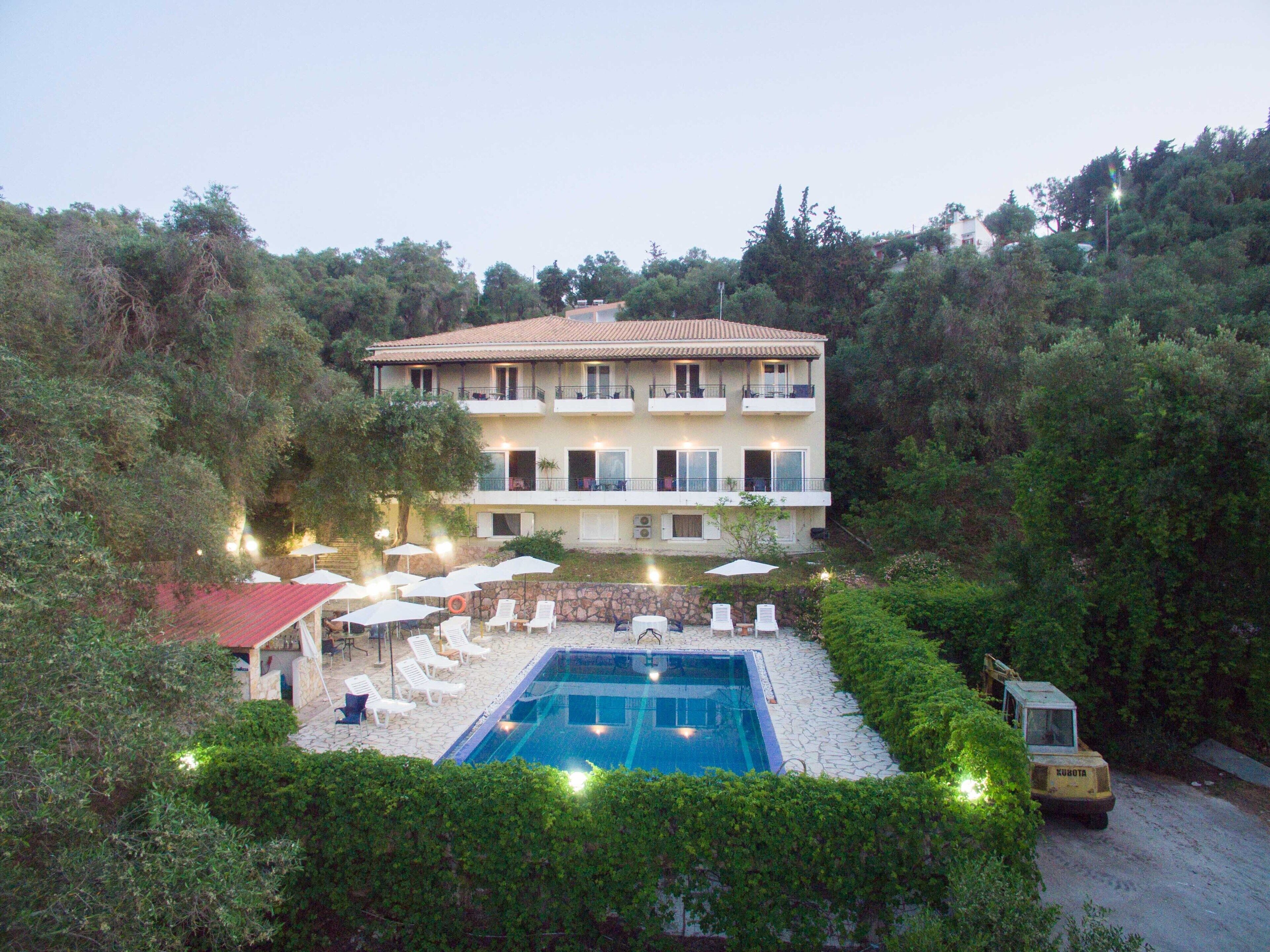 A two-story building with a swimming pool, surrounded by lush greenery and trees.