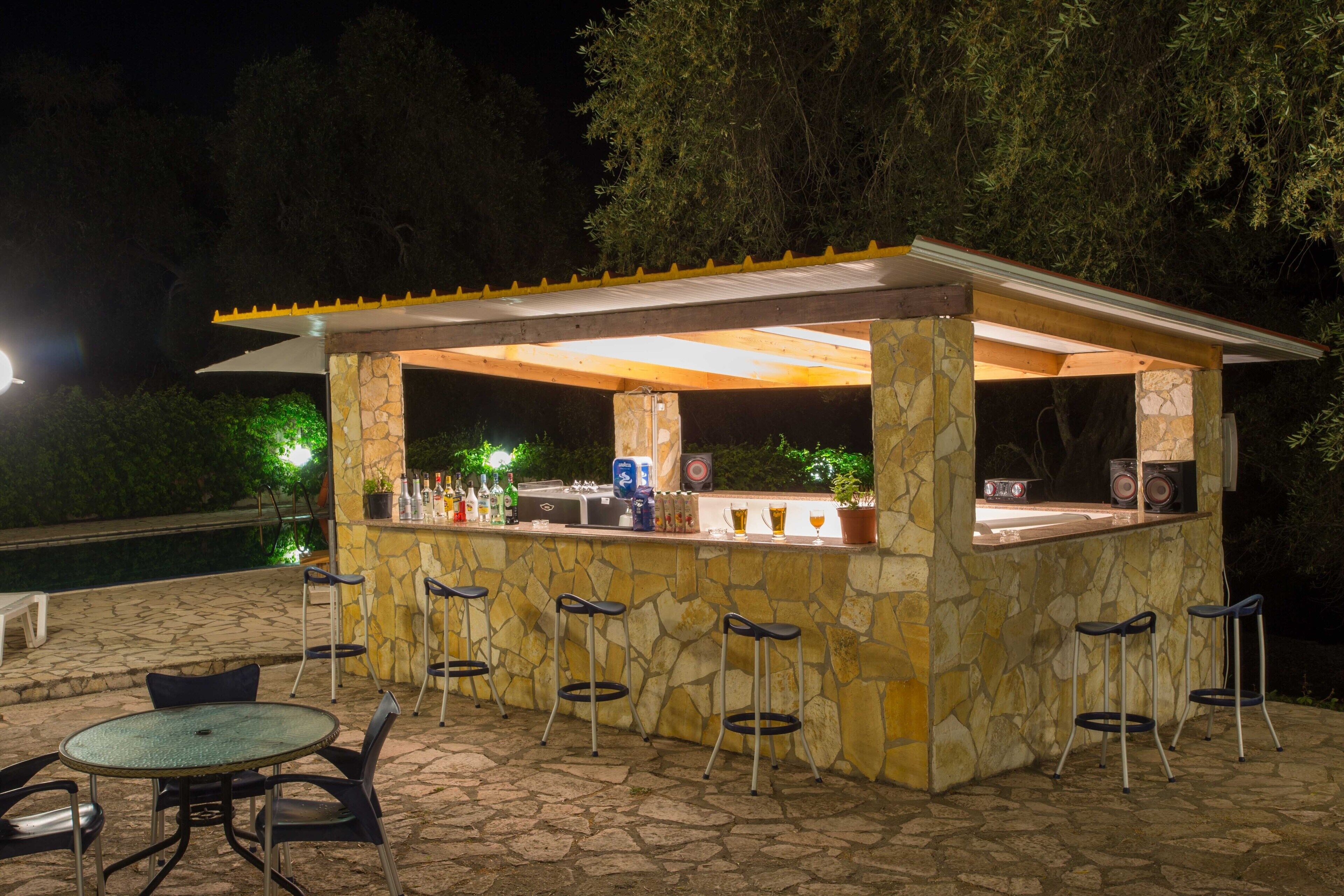 Un espace bar extérieur avec des murs en pierre, des tabourets de bar et une piscine en arrière-plan.