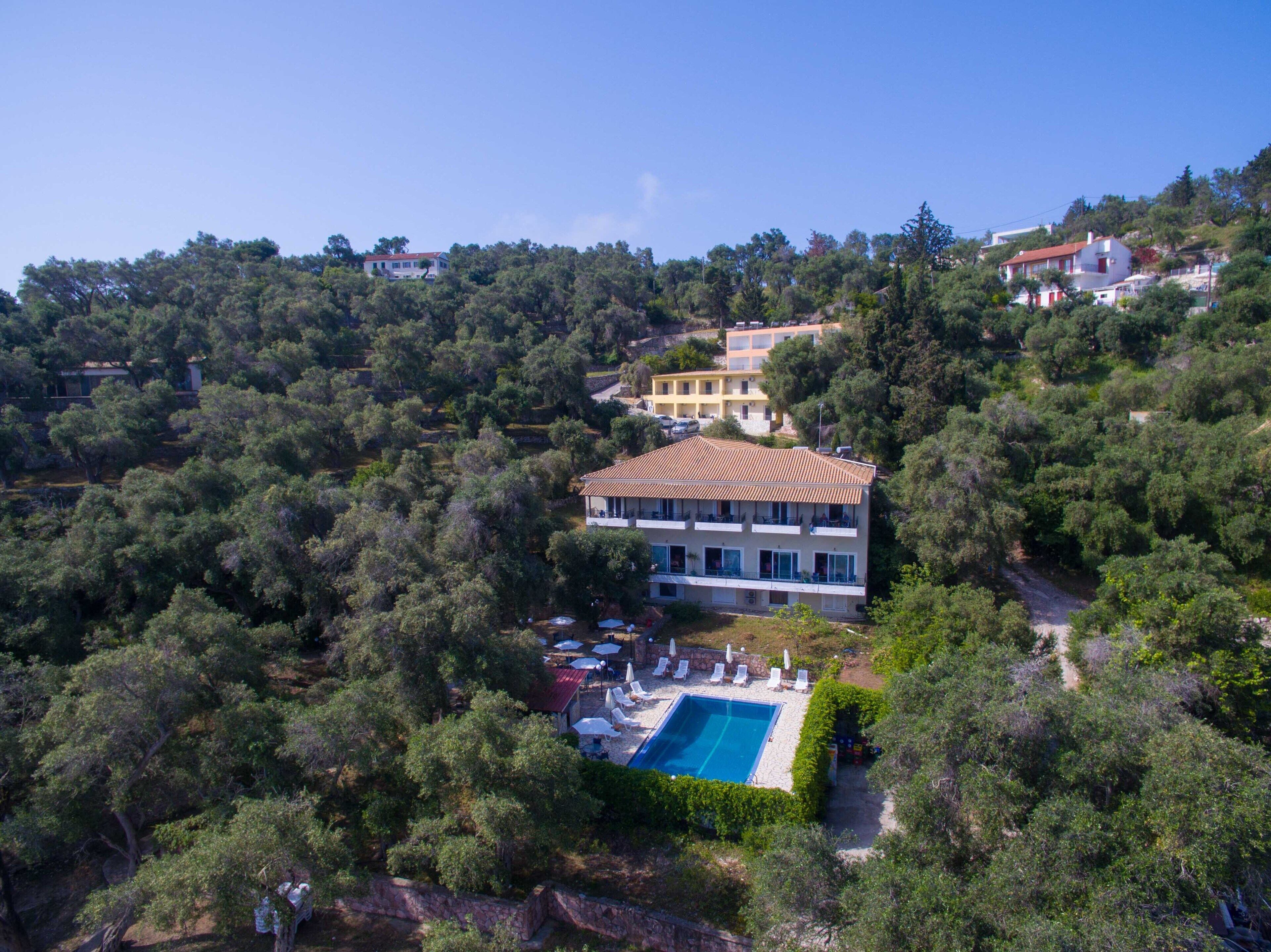 Vue aérienne d’une propriété située sur une colline, avec un grand bâtiment doté d’une piscine et d’un espace de détente extérieur.