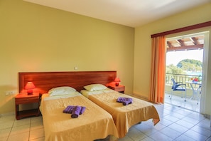 A hotel room with two beds, a wooden headboard, a balcony with a table and chairs, and a view of the outdoors. - Amfitriti Hotel (Paxos)