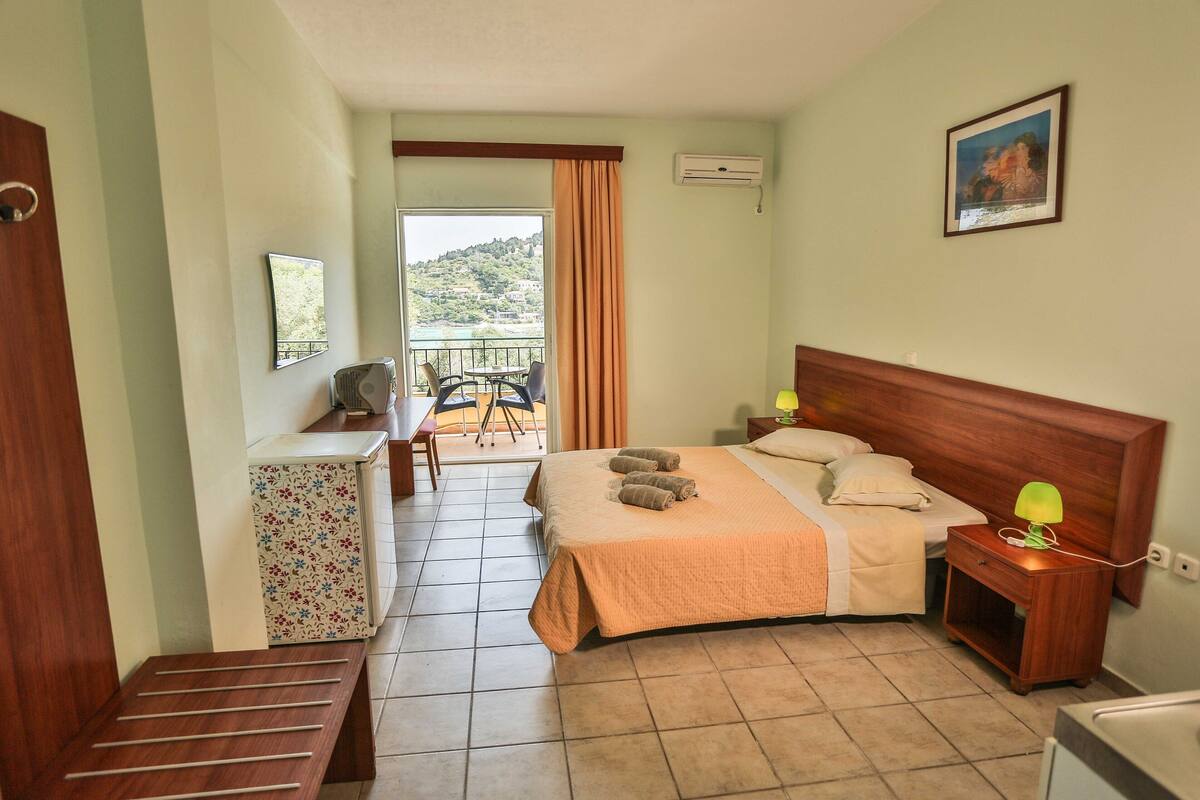 Ein Hotelzimmer mit Bett, Nachttisch und Blick auf einen Balkon mit Tisch und Stühlen.