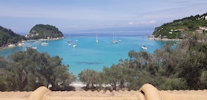 A coastal view with boats on turquoise waters, surrounded by hills and sparse vegetation. - Amfitriti Hotel (Paxos)