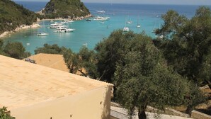 A coastal view with boats anchored in turquoise waters, surrounded by greenery and a hillside. - Amfitriti Hotel (Paxos)