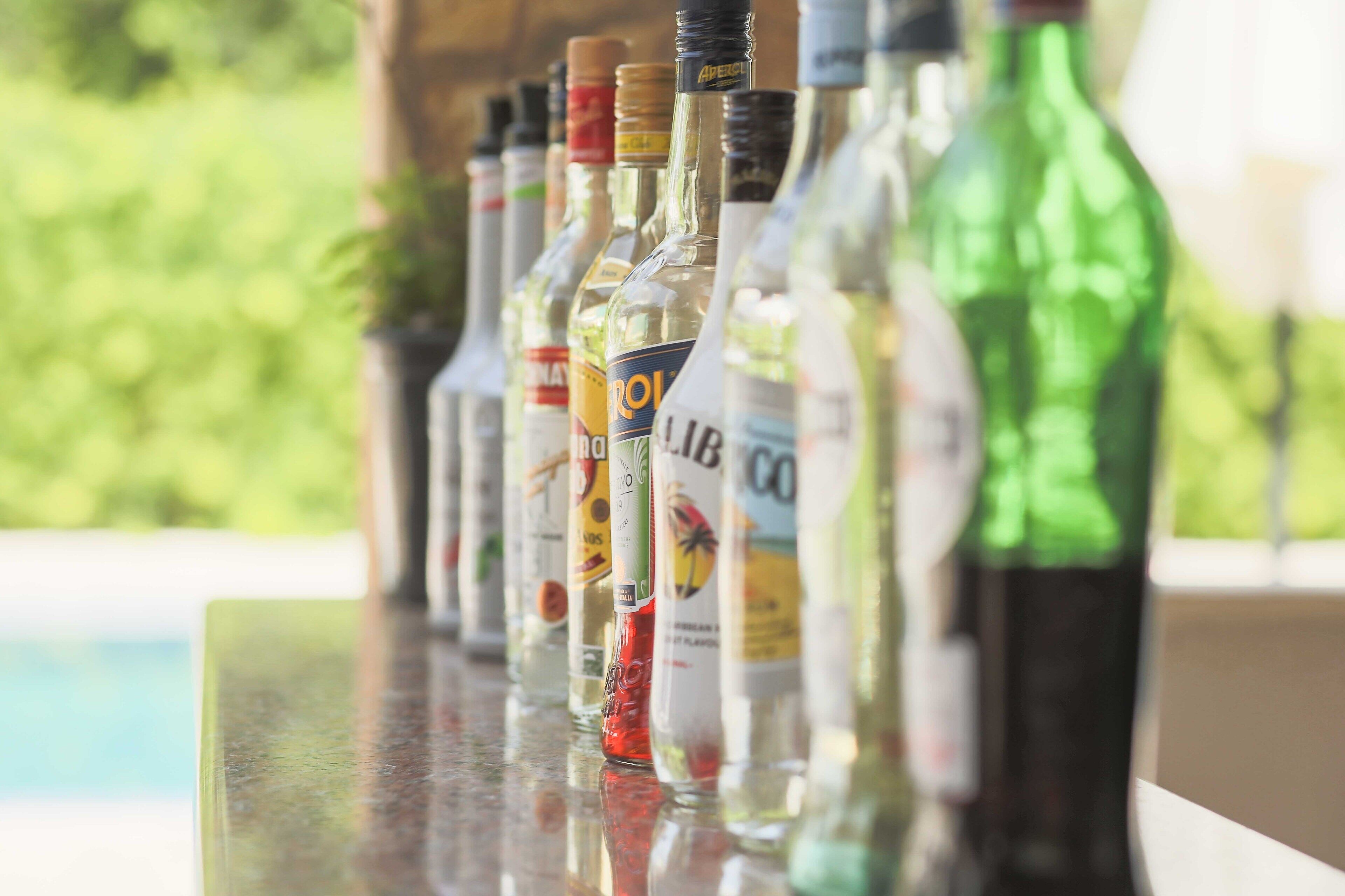 A row of liquor bottles on a bar counter with a pool in the background.