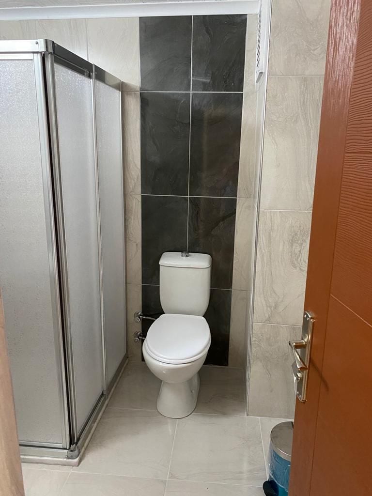 A bathroom with a toilet, a shower enclosure, and a tiled floor.