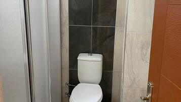 A bathroom with a toilet, a shower enclosure, and a tiled floor.