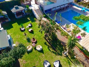 An aerial view of a modern hotel with a swimming pool, outdoor seating, and a well-maintained lawn.