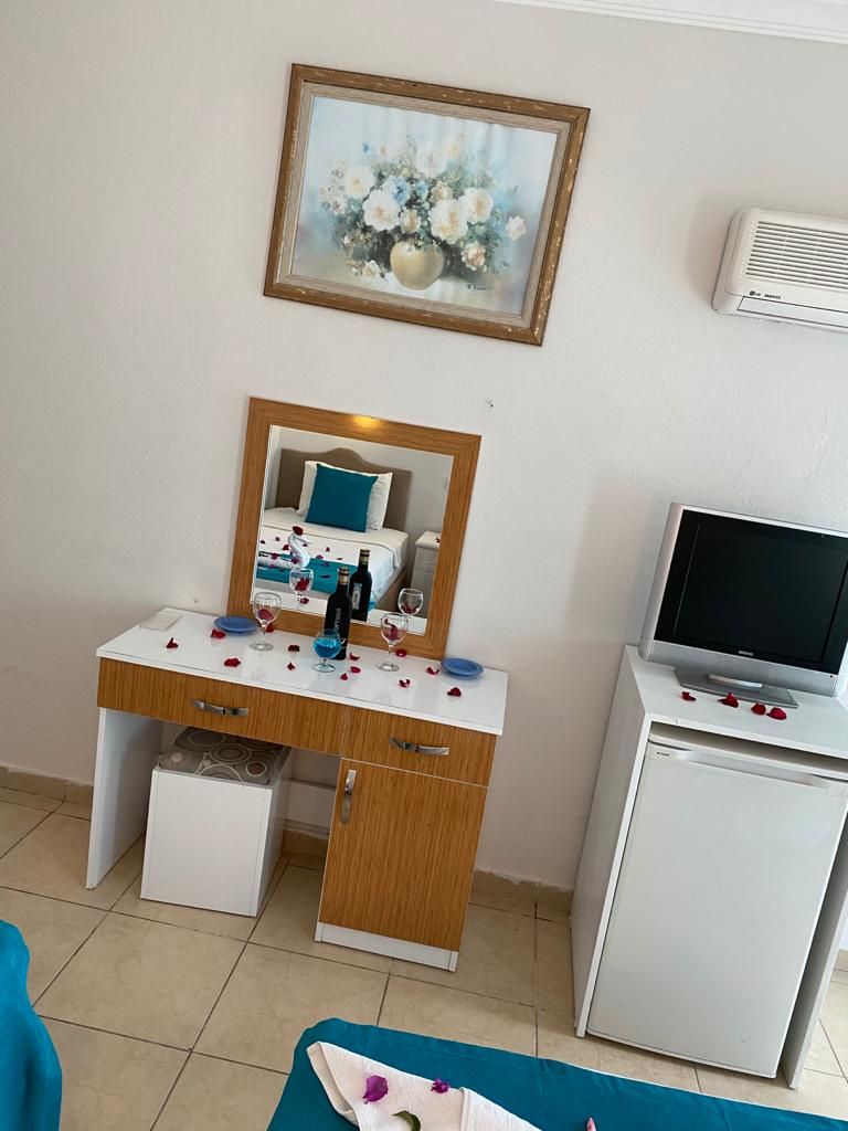 Una habitación con tocador, espejo, televisor y un cuadro en la pared.