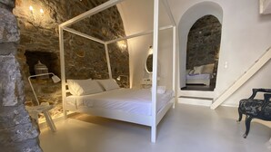 A four-poster bed in a stone-walled bedroom with a staircase leading to an upper level. - Lida Mary (Chios)