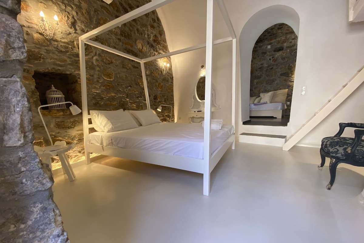 Una cama con dosel en un dormitorio con paredes de piedra y una escalera que lleva a un nivel superior.