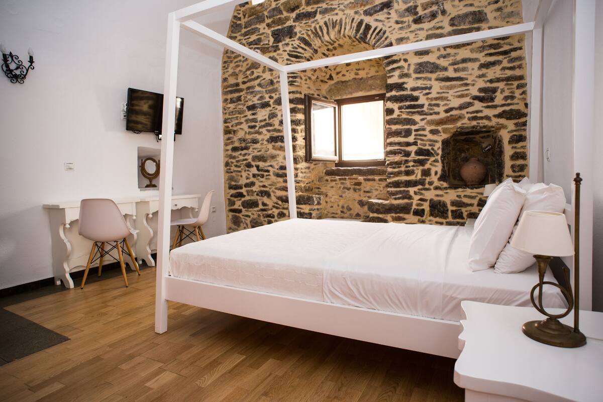 Un dormitorio con pared de piedra, una cama, un escritorio y una silla.
