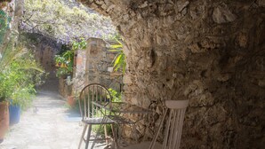 A stone-walled patio with a table and chairs, surrounded by potted plants and a view of a garden. - Lida Mary (Chios)