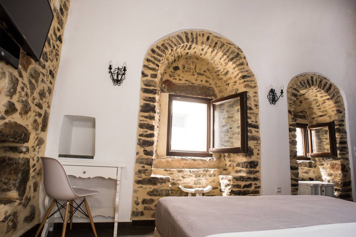 Un dormitorio con paredes de piedra, una cama, un escritorio y una silla.