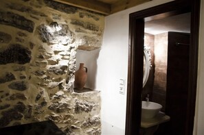 Un baño con pared de piedra, un lavabo blanco y una puerta de madera.