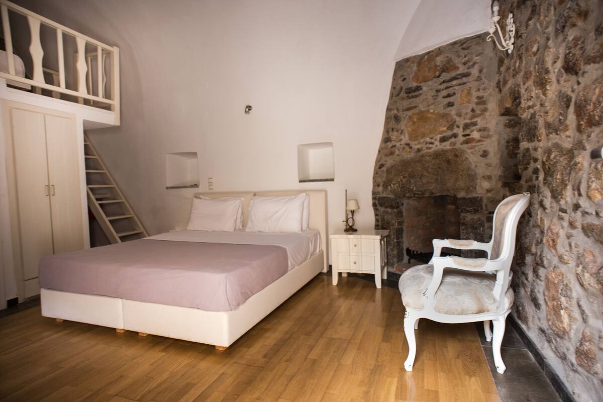 Un dormitorio con cama, mesita de noche, silla, cómoda y pared de piedra.