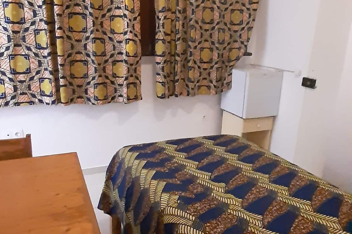 Ein Zimmer mit einem Bett, das mit gemusterten Textilien bezogen ist, einem Holztisch und Vorhängen mit geometrischem Muster.