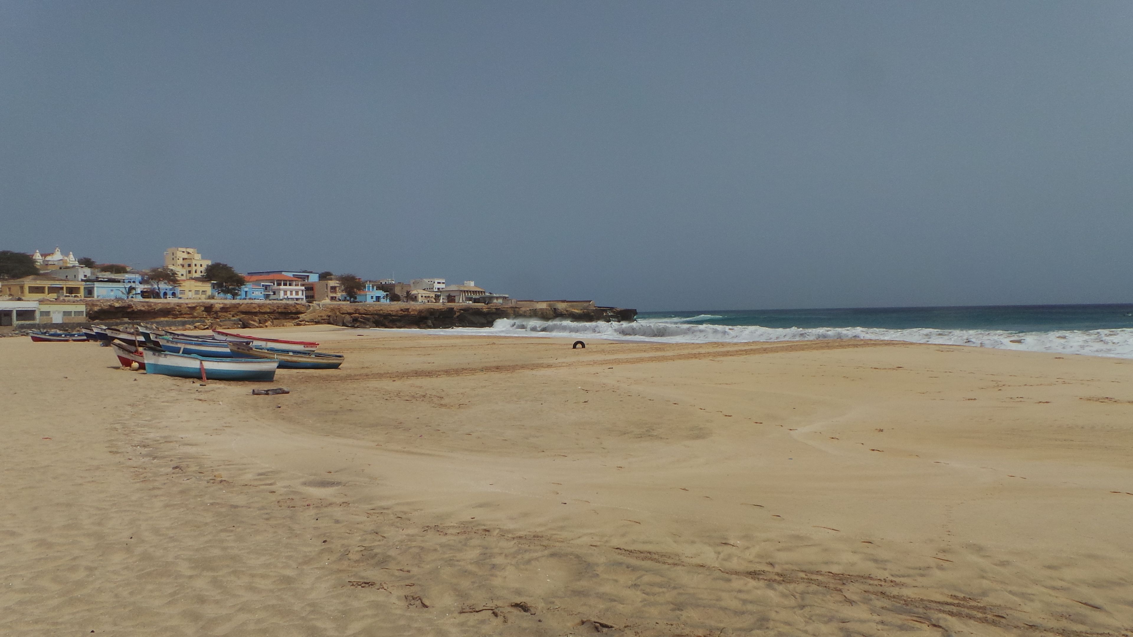 A sandy beach with several boats lined up near the shore.