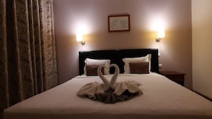 A neatly made bed with a swan-shaped towel arrangement, two pillows, and two wall-mounted lights.