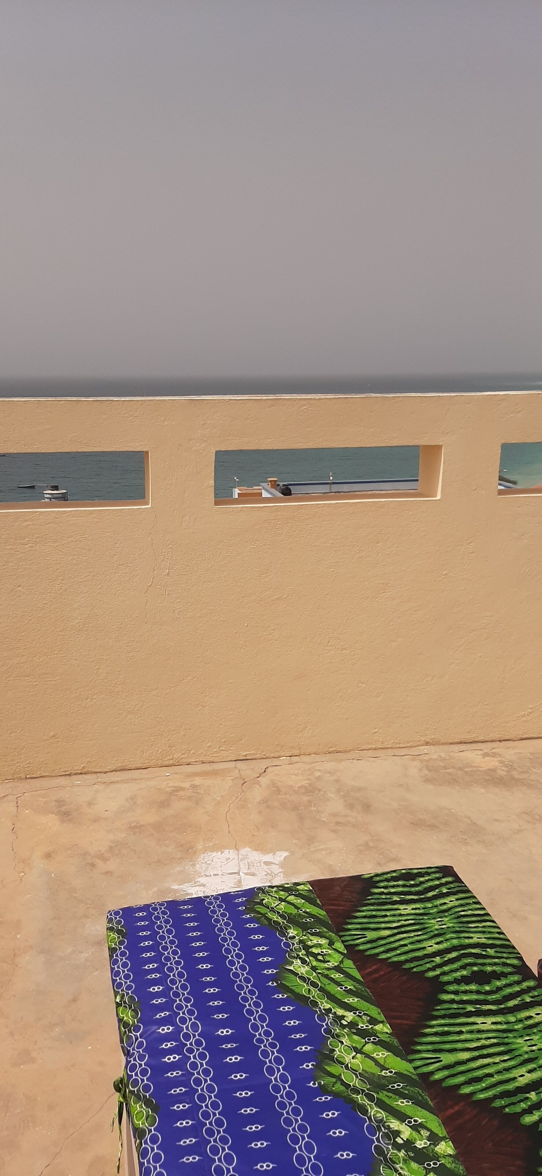 A beach view with a blue patterned mat and a beige wall with three windows.
