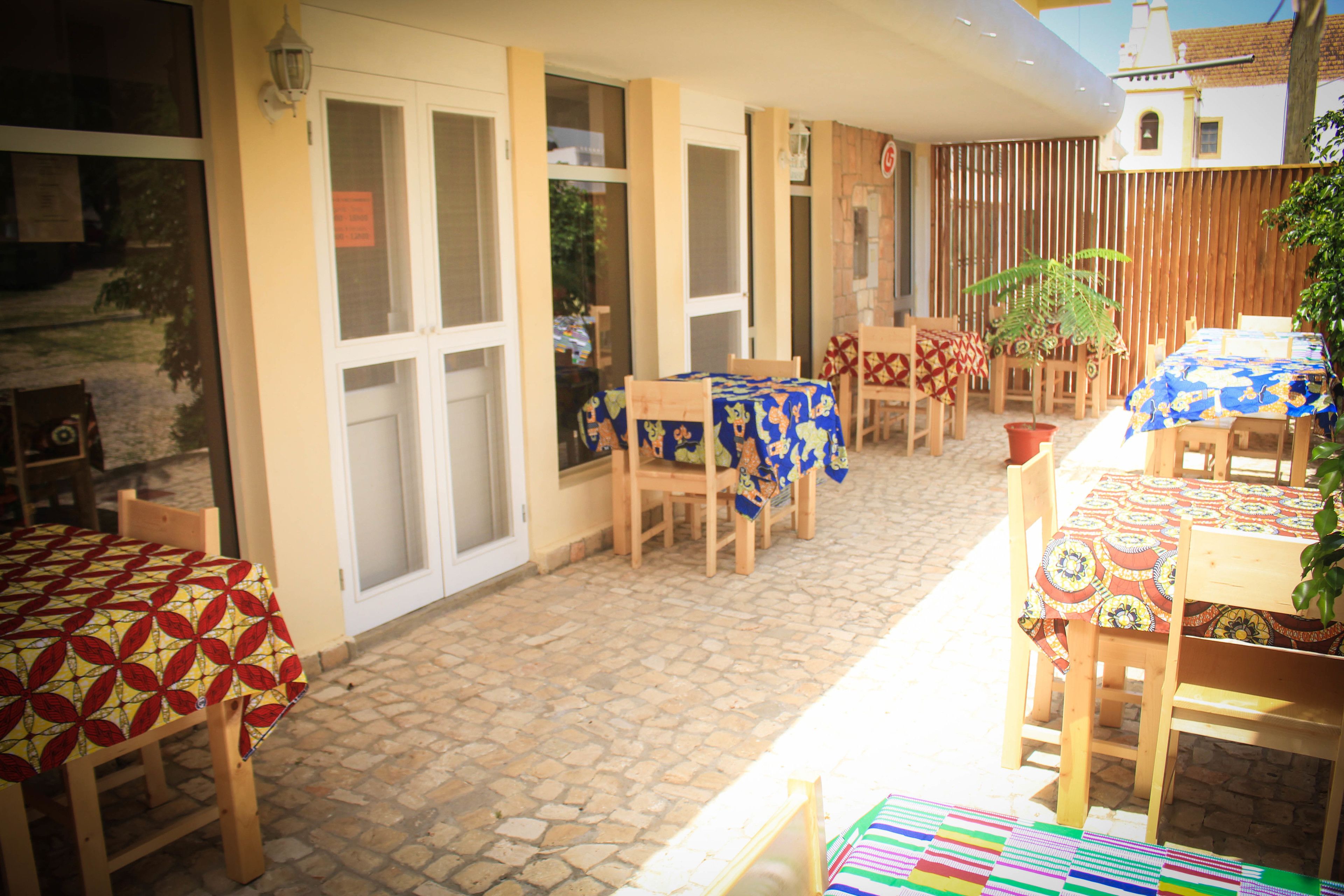 An outdoor patio area with tables and chairs, some with tablecloths, and potted plants.