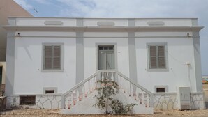 A white building with a central door, two windows on either side, and a staircase leading up to the entrance.