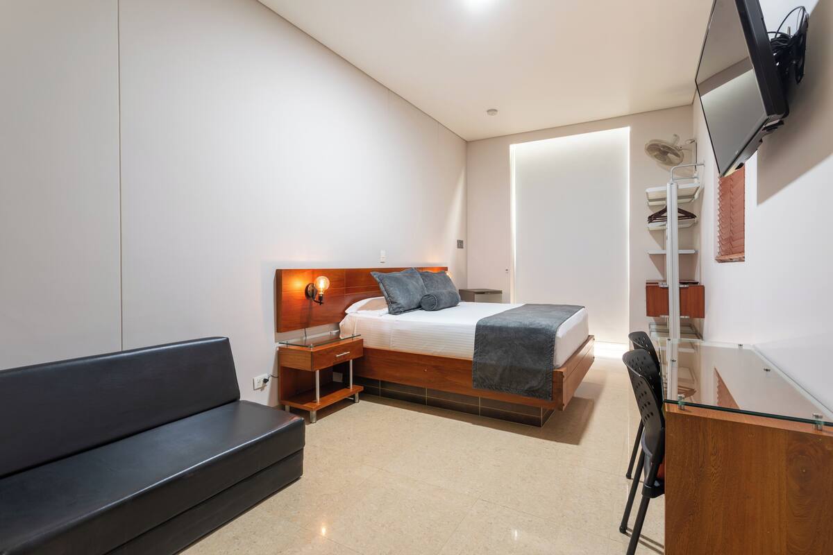 A modern bedroom with a bed, bedside table, lamp, and a TV mounted on the wall.
