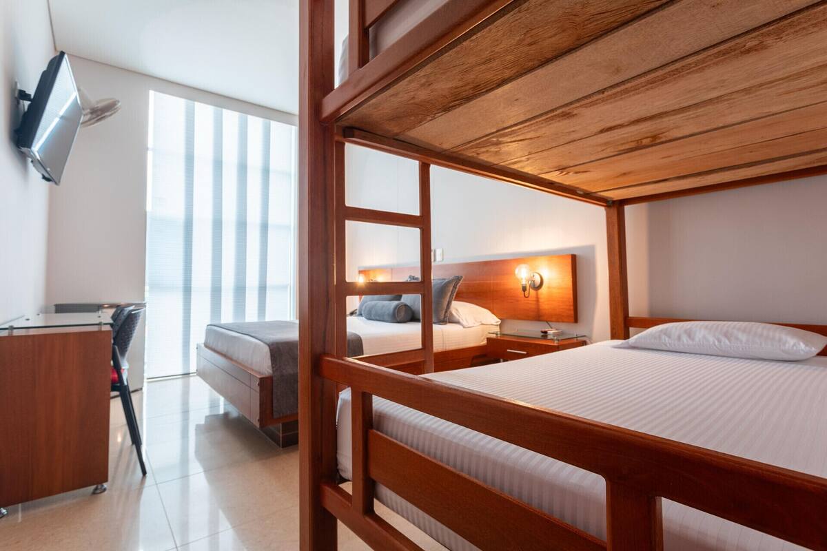 A hotel room with a wooden bed, a desk, and a TV mounted on the wall.
