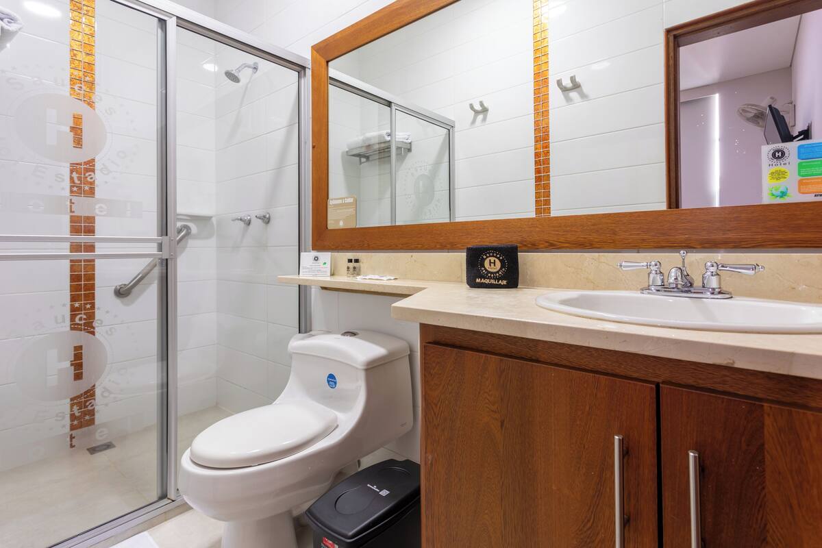 A modern bathroom with a glass shower enclosure, a white toilet, a wooden vanity with a sink, and a large mirror above the vanity.