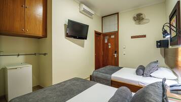 A hotel room with two single beds, a television, an air conditioning unit, a small refrigerator, and a wooden wardrobe.